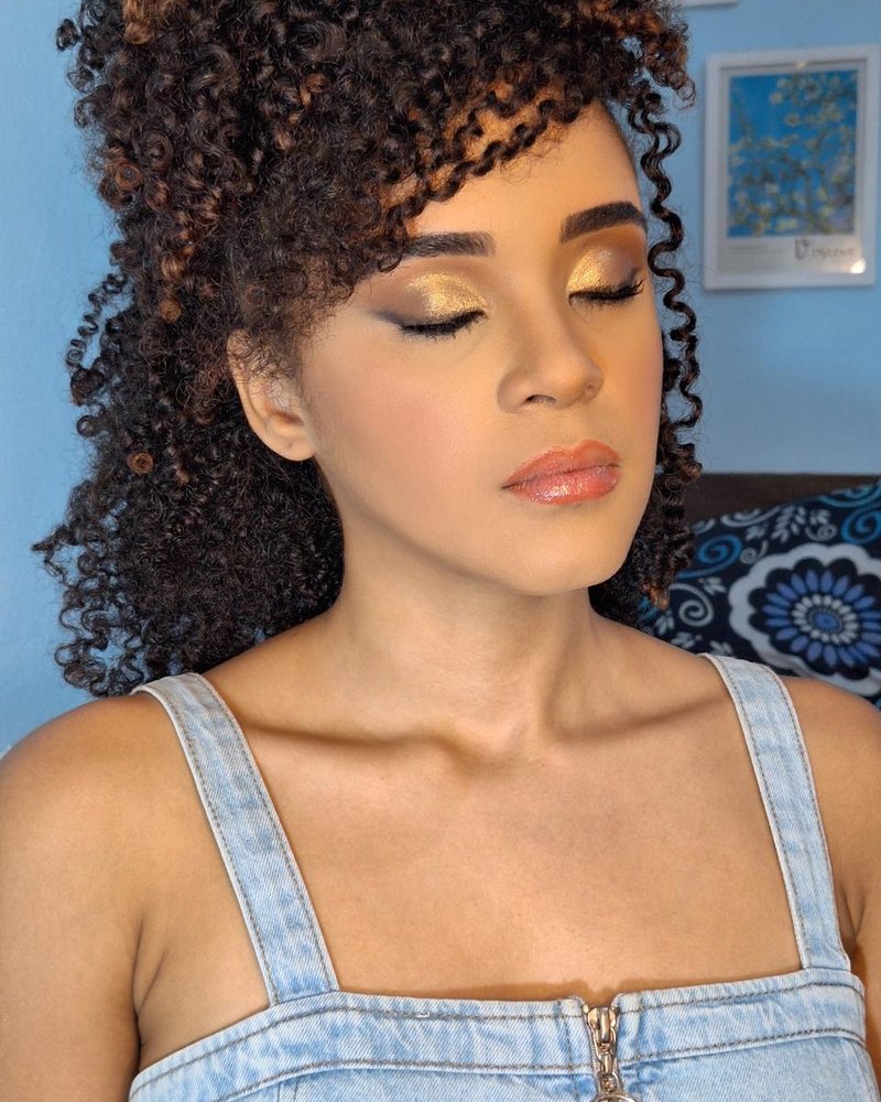 Maquiagem dourada com pele iluminada em cliente jovem de cabelo cacheado, por Maria Eduarda Lima